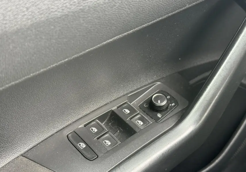 Gros plan sur les commandes de lève-vitres et réglage des rétroviseurs côté conducteur d'une Volkswagen Polo bleu 2021.