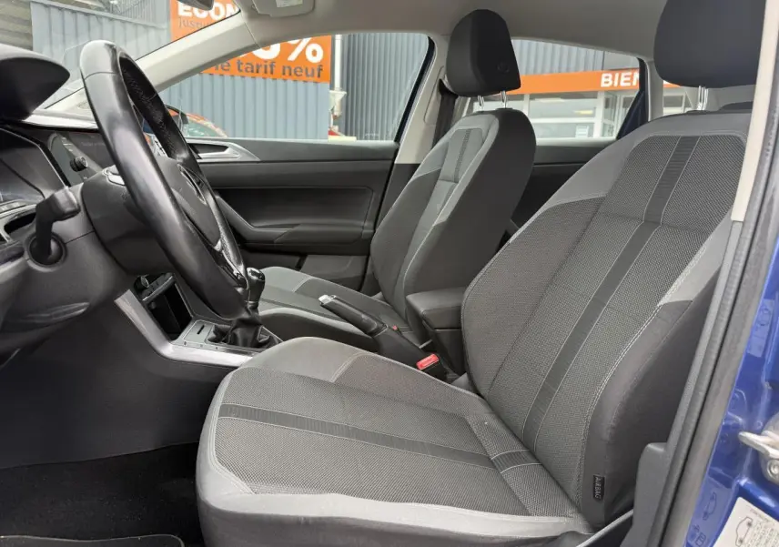 Intérieur avant de la Volkswagen Polo bleu 2021, sièges sport tissu gris avec volant et levier de vitesse manuels visibles.