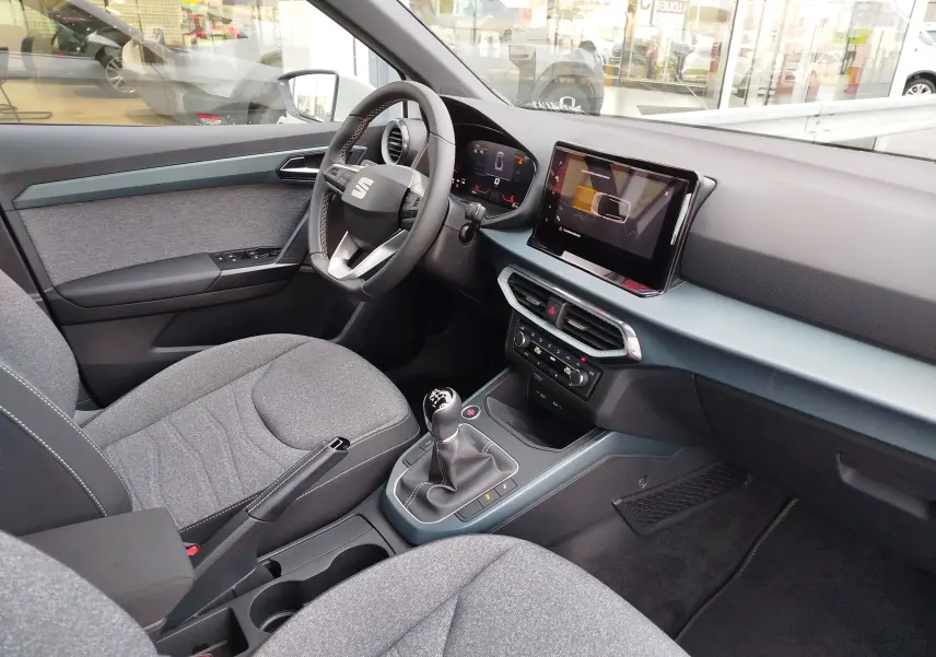 Vue intérieure côté conducteur du SEAT Arona 2023, mettant en valeur le tableau de bord moderne et les sièges gris en tissu.