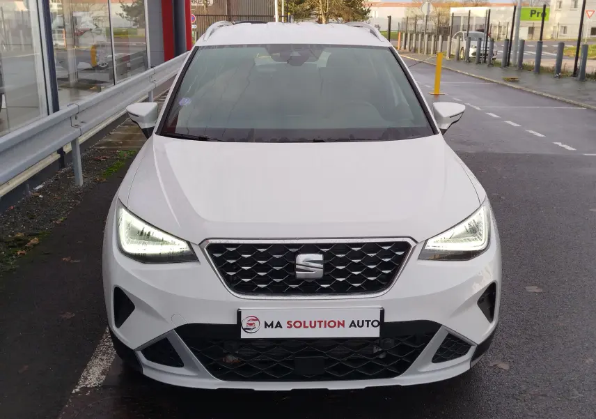 Vue avant d'un SEAT Arona blanc Candy 2023 avec phares LED allumés et calandre noire ajourée.