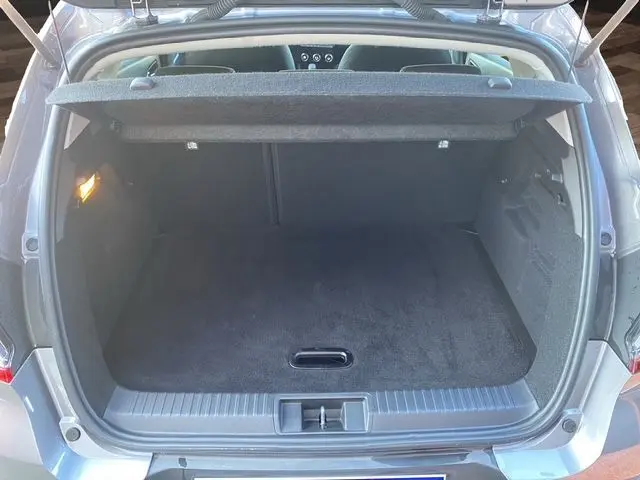 Coffre ouvert vu de l'arrière d'un Renault Captur E-Tech Full Hybrid 145 gris Cassiopée, intérieur noir et tapis propre.