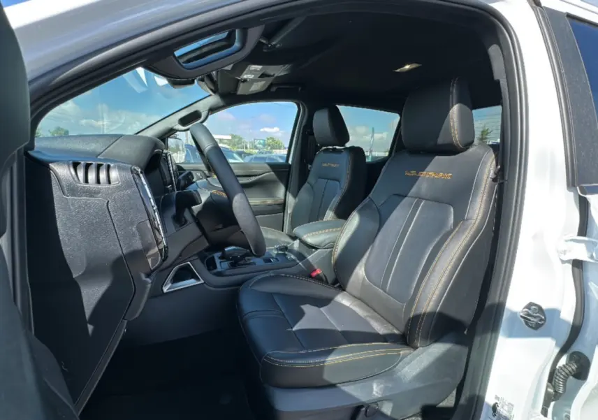 Vue intérieure côté conducteur du Ford Ranger blanc 2.3 PHEV Wildtrak avec sièges cuir noirs et surpiqûres orange.