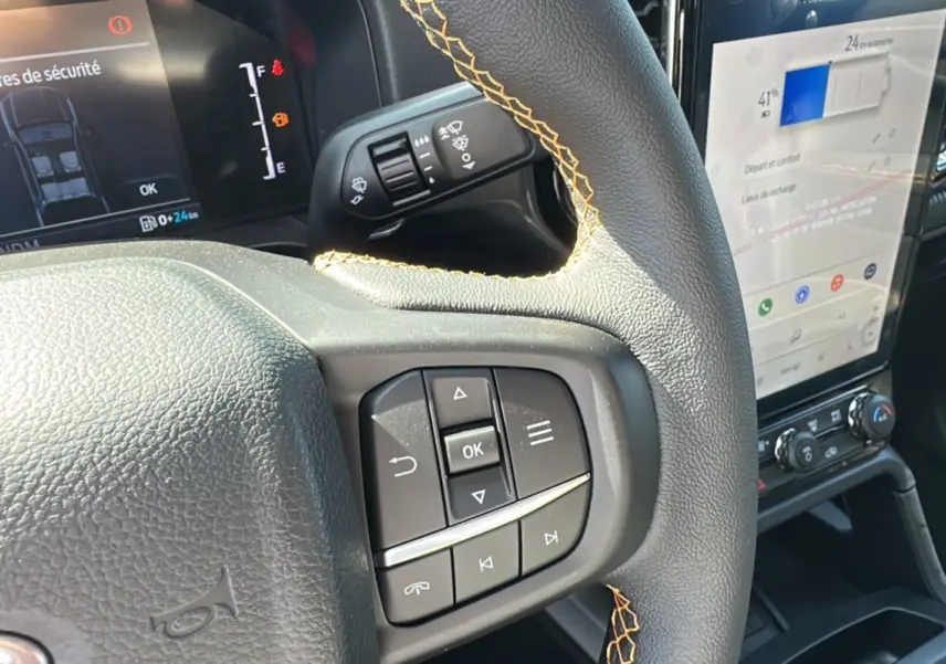 Gros plan sur le volant cuir noir avec surpiqûres jaunes du Ford Ranger blanc, affichage numérique et écran tactile central visibles.