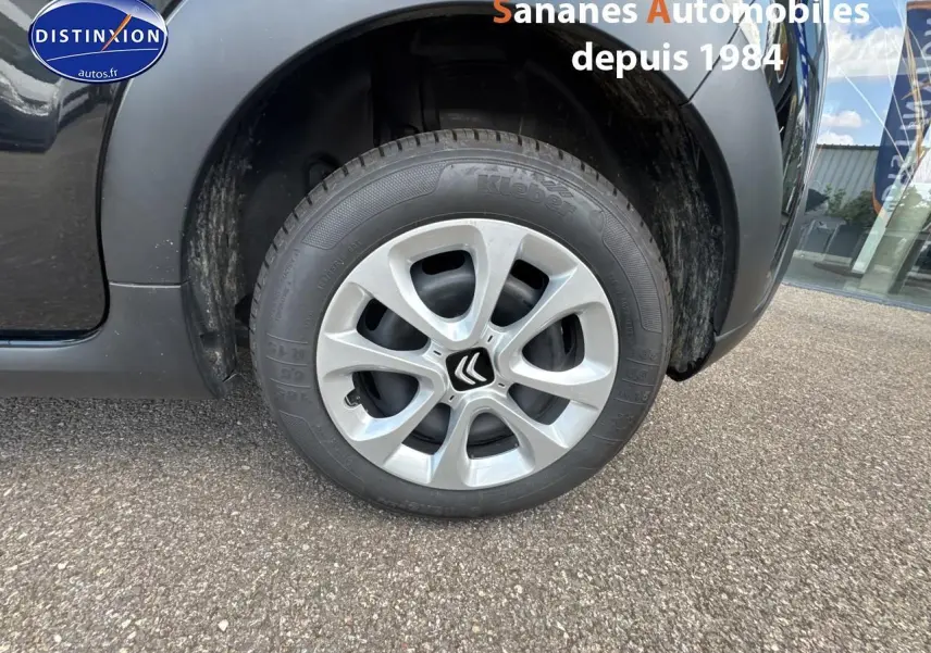 Gros plan sur la roue avant droite d'une Citroën C3 noire 2023 avec jante argentée et logo Citroën central.