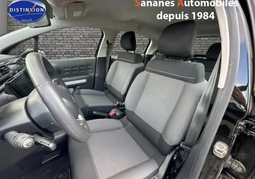 Vue intérieure côté conducteur de la Citroën C3 noire 2023, sièges tissu gris avec surpiqûres jaunes visibles.