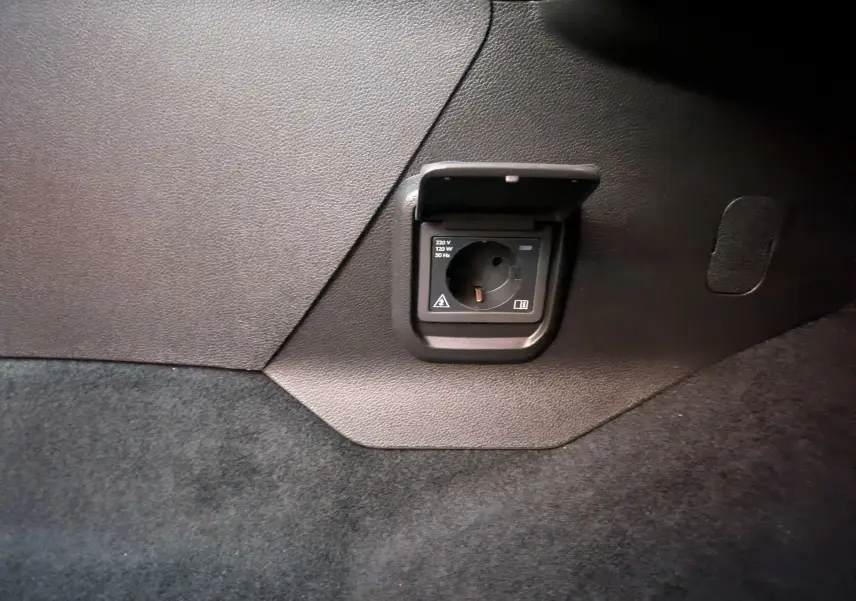 Prise électrique 220V intégrée dans le panneau intérieur noir du coffre du Peugeot Rifter gris Artense 2025.