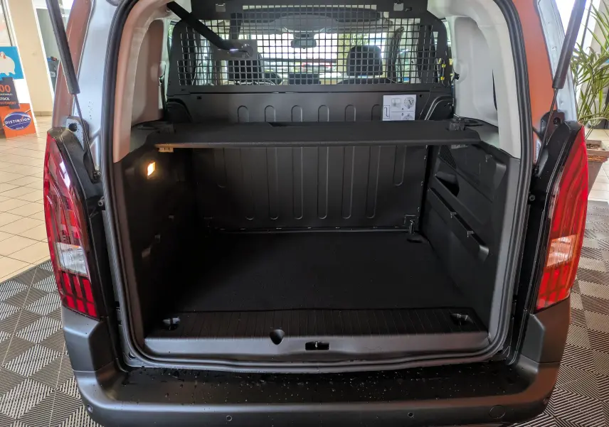 Coffre ouvert vu de l'arrière du Peugeot Rifter gris Artense 2025, avec séparation grillagée et éclairage intérieur.