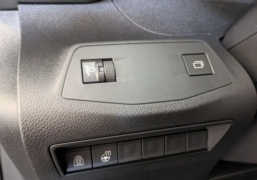 Gros plan sur les commandes de réglage des phares et du volant chauffant dans l’habitacle noir du Peugeot Rifter 2025.