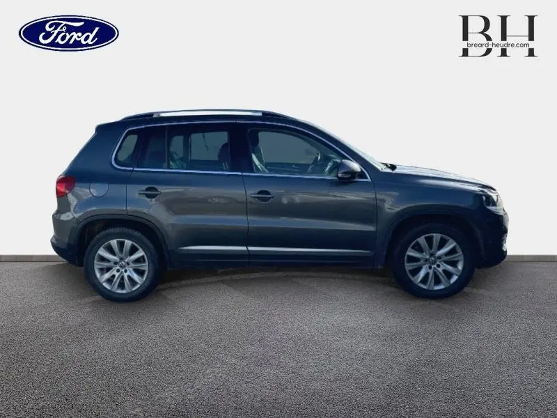 Vue de profil côté gauche d'un Volkswagen Tiguan gris Crypton avec jantes alliage et barres de toit visibles.