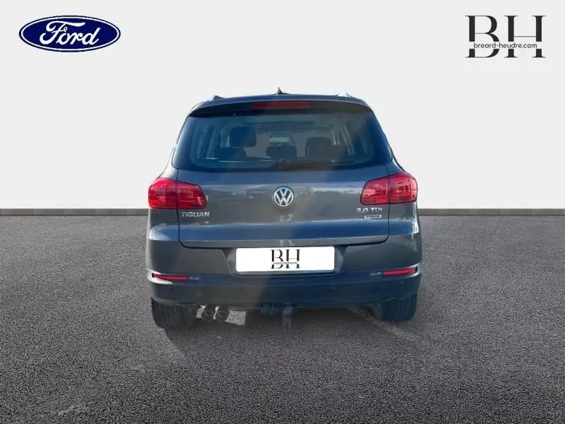 Vue arrière d'un Volkswagen Tiguan gris Crypton 2016 avec feux rouges et attelage visible sur un sol goudronné.