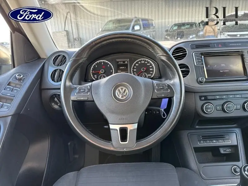 Vue intérieure centrée sur le volant Volkswagen d'un Tiguan 2016, avec tableau de bord et écran tactile visibles.