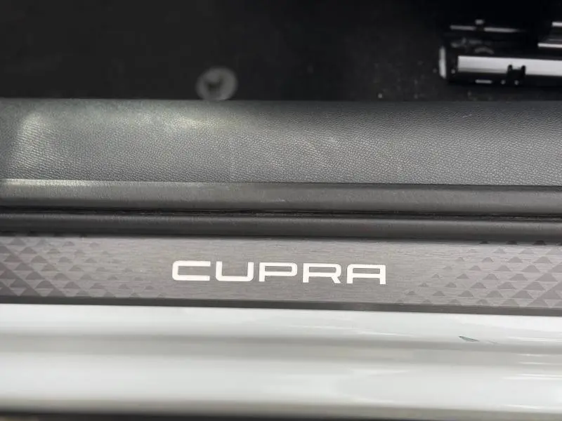 Gros plan sur la signature CUPRA sur la porte d’un Formentor blanc Nevada métallisé, intérieur noir visible en arrière-plan.