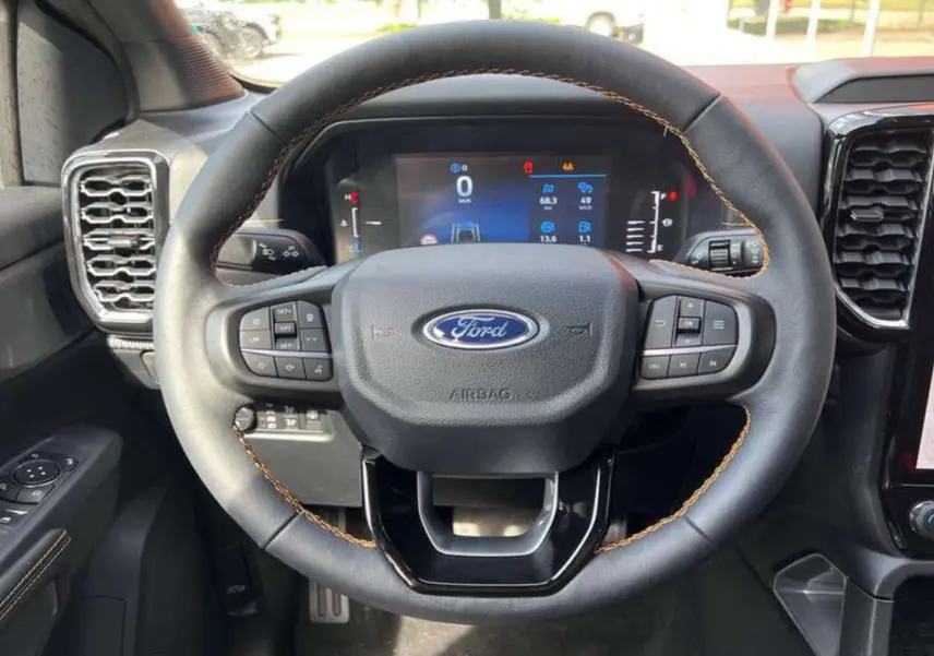Vue rapprochée du volant cuir noir avec surpiqûres marron du Ford Ranger 2026, tableau de bord numérique visible.