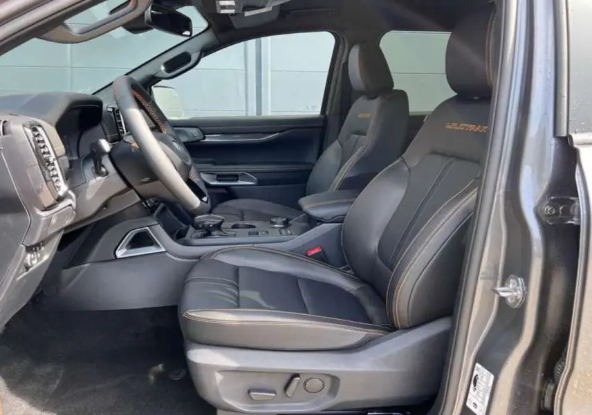 Vue intérieure côté conducteur du Ford Ranger noir agate 2026, sièges cuir Wildtrak avec surpiqûres orange visibles.