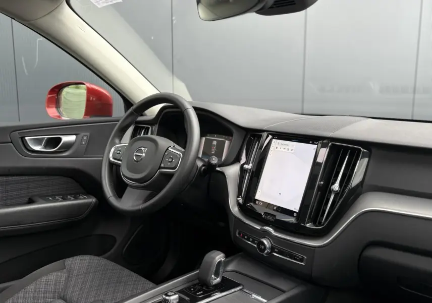 Vue intérieure côté conducteur du Volvo XC60 rouge Fusion 2024, avec tableau de bord digital et écran tactile vertical.