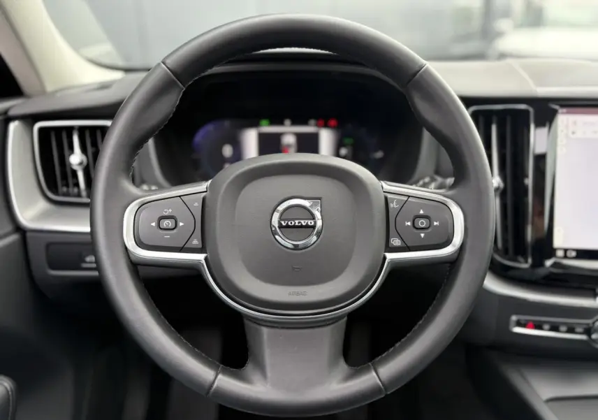 Volant simili-cuir noir de Volvo XC60 2024 vu de face avec commandes intégrées et tableau de bord digital flou.