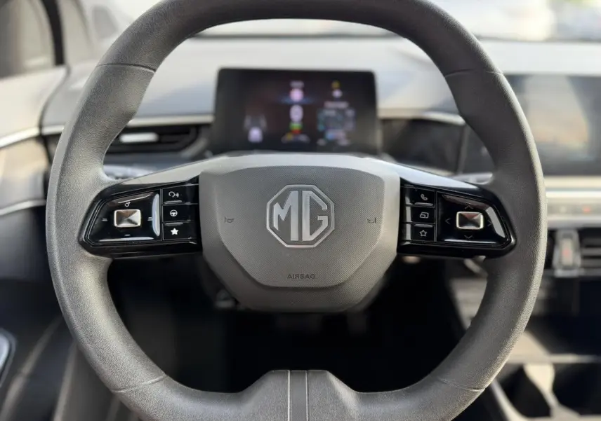 Vue centrée sur le volant noir du MG3 1.5 Hybrid+ 195 Comfort, avec commandes intégrées et tableau de bord flou en arrière-plan.
