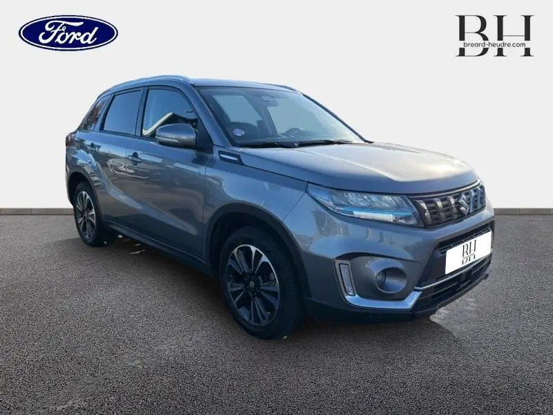 Suzuki Vitara Galactic Gray métallisé en 3/4 avant droit, mettant en valeur sa calandre chromée et ses jantes alu noires.