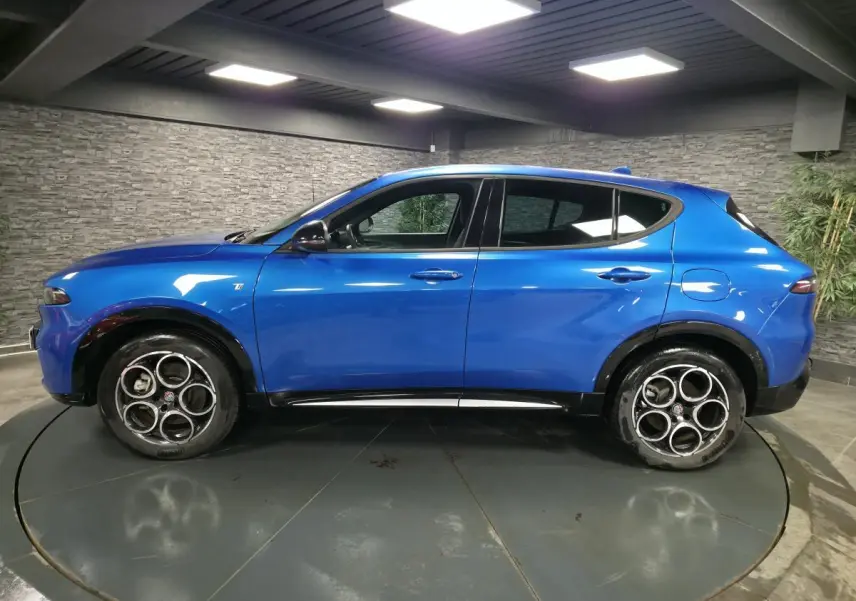 Profil latéral gauche de l'Alfa Romeo Tonale 1.3 PHEV bleu métallisé avec rétroviseurs noirs brillants en intérieur.