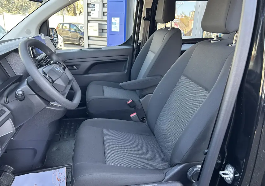 Vue intérieure côté conducteur du Citroën Jumpy Cabine Approfondie noir, montrant les sièges tissu gris et le volant.