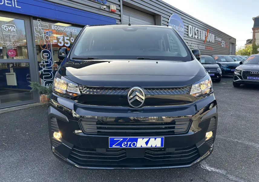 Vue de face d'un Citroën Jumpy Cabine Approfondie noir avec projecteurs allumés sur un parking de concession.