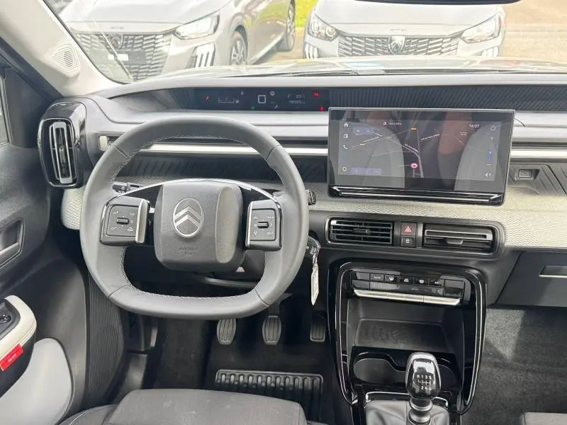Vue intérieure avant du tableau de bord de la Citroën C3 2025 gris Mercury avec volant multifonction et écran tactile central.