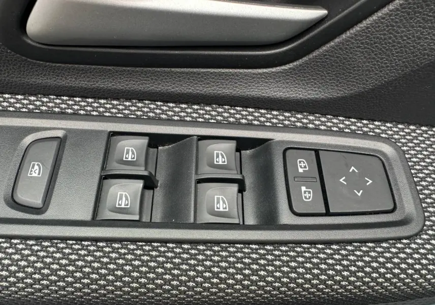Gros plan sur les commandes des vitres électriques et réglages des rétroviseurs sur la porte côté conducteur du Dacia Jogger Vert Cèdre.