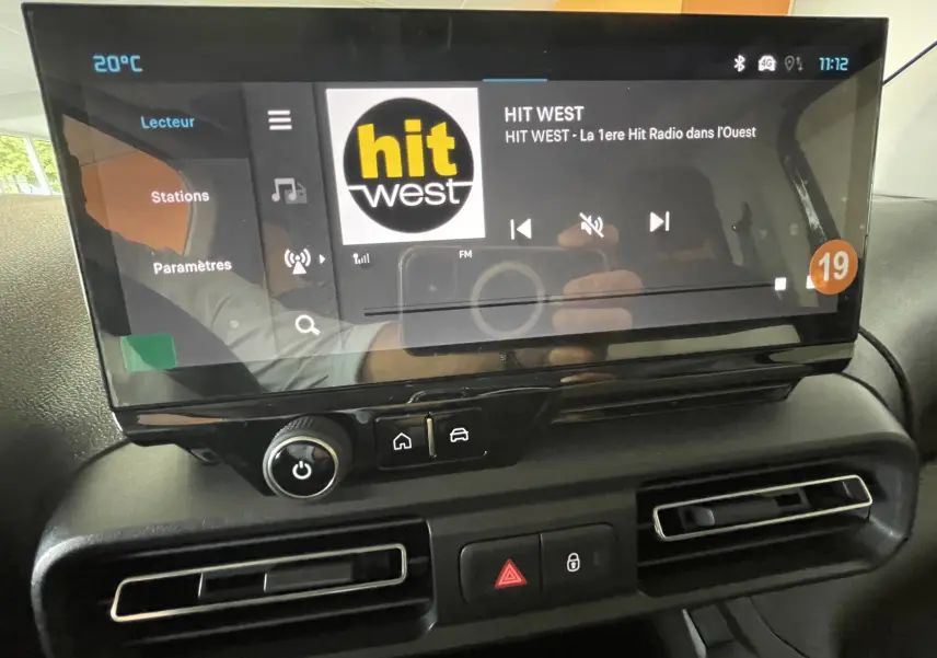 Écran tactile central du tableau de bord du Citroën Berlingo noir 2025 affichant la radio Hit West et commandes climatisation.