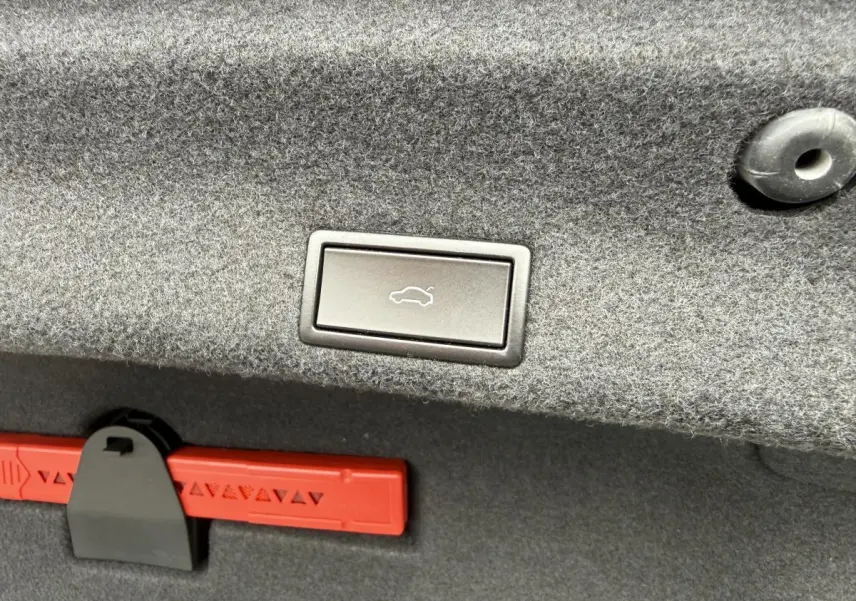 Bouton d'ouverture électrique du coffre sur la garniture grise du coffre d'une Volkswagen Passat noire 2018.