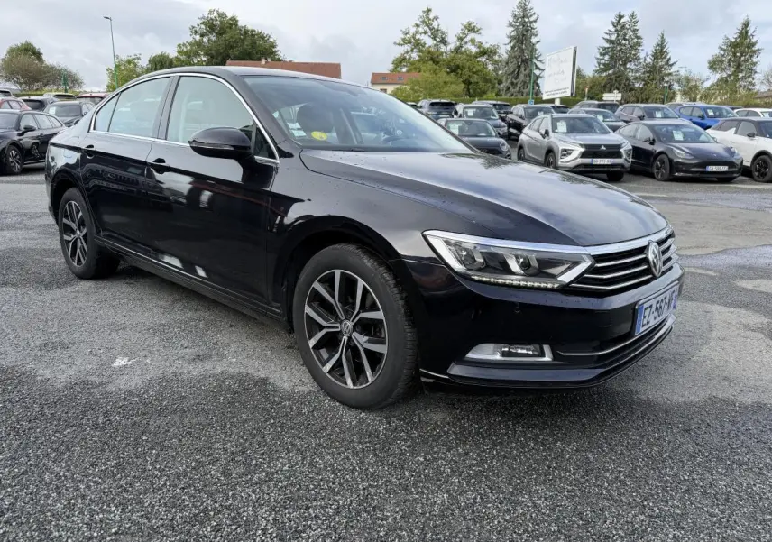 Volkswagen Passat noire vue 3/4 avant droit, avec jantes alliage et calandre chromée sur parking.