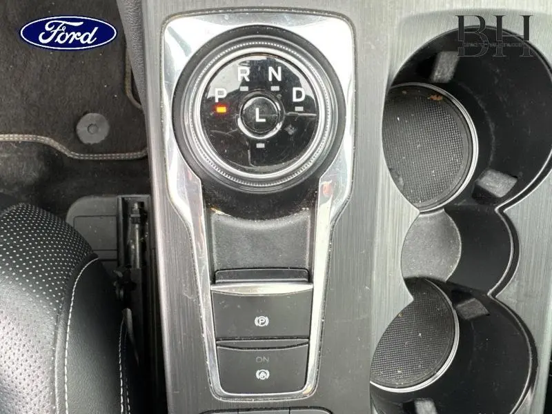 Vue rapprochée de la commande de boîte automatique circulaire et porte-gobelets sur la console centrale noire du Ford Kuga bleu azur.