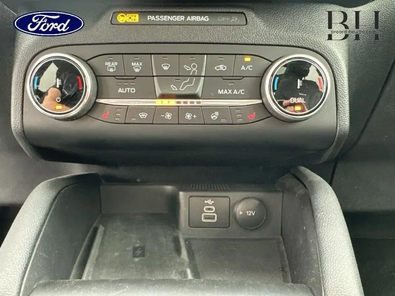 Vue rapprochée de la console centrale du Ford Kuga bleu azur, montrant les commandes de climatisation et prises USB et 12V.