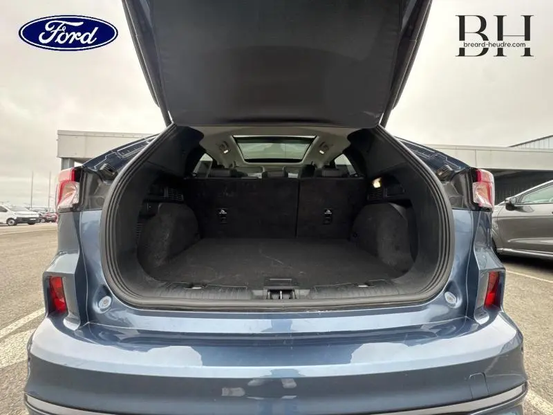 Vue arrière du coffre ouvert d'un Ford Kuga bleu azur métallisé avec toit panoramique visible depuis l'intérieur