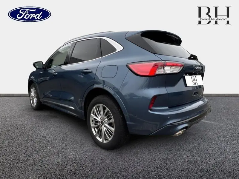 Ford Kuga bleu azur métallisé vu en 3/4 arrière droit avec toit panoramique et jantes alu brillantes.