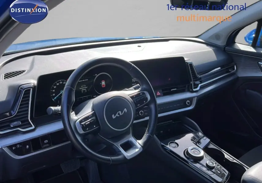 Vue intérieure du poste de conduite du Kia Sportage bleu fusion métal 2022, avec volant cuir multifonction et écran digital large.