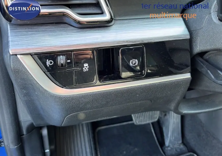 Détail du tableau de bord côté gauche du Kia Sportage bleu fusion métal 2022, montrant les commandes d’éclairage et frein à main électrique.