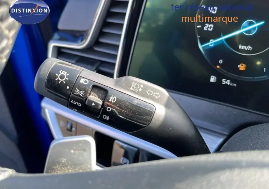 Gros plan sur la commande des feux et clignotants du Kia Sportage bleu fusion, avec tableau de bord digital affichant 54 km.