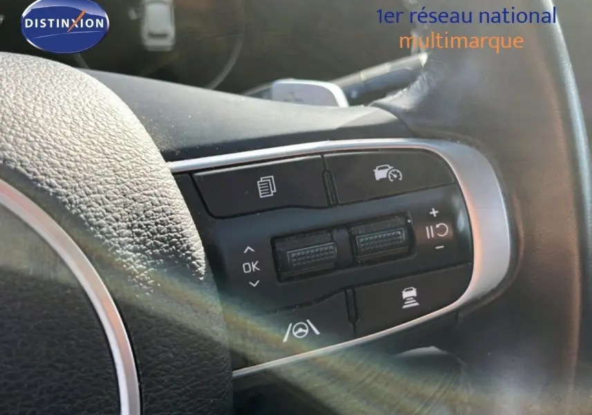 Gros plan sur les commandes au volant en cuir noir du KIA Sportage 2022, boutons de régulateur de vitesse visibles.