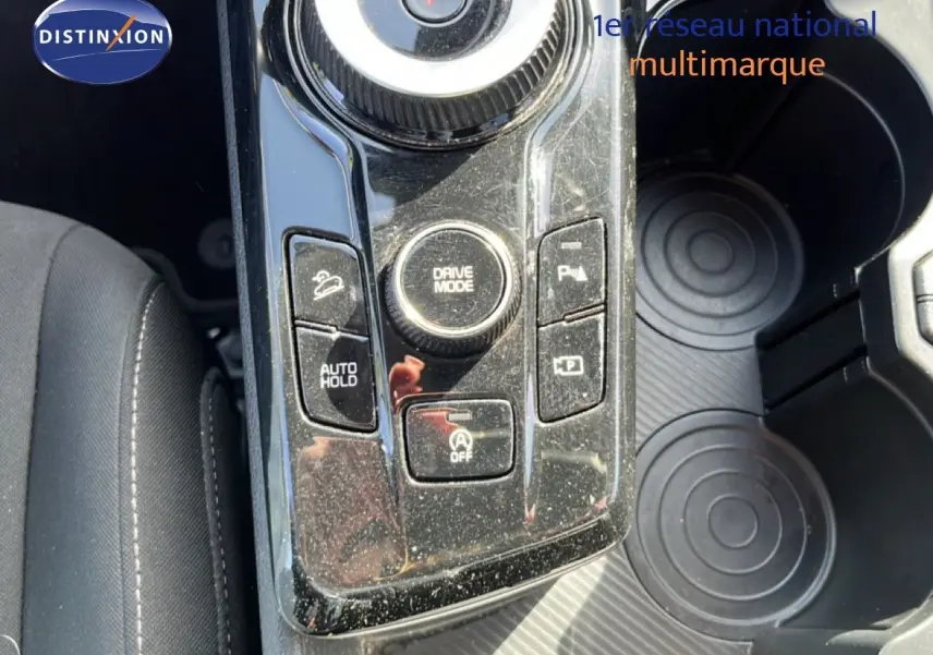 Gros plan sur la console centrale du Kia Sportage 2022, montrant les commandes de mode de conduite et maintien auto, avec porte-gobelets.