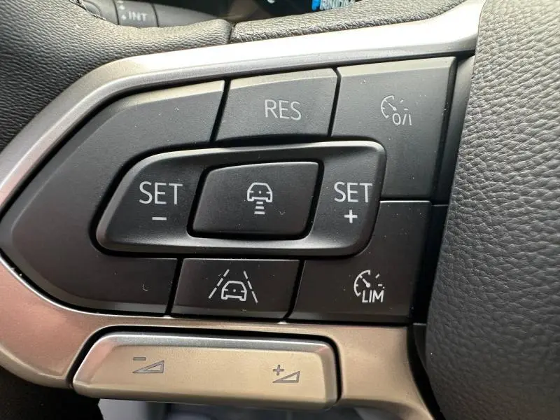 Gros plan sur les commandes au volant cuir noir du Volkswagen Transporter FGN gris, boutons de régulateur et assistance conduite.