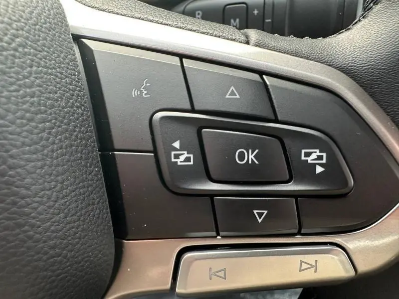 Gros plan sur les commandes multifonctions noires du volant cuir du Volkswagen Transporter FGN gris 2025.