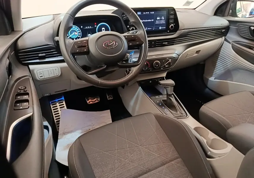 Vue intérieure avant de la Hyundai Bayon 2023, tableau de bord gris avec écran tactile et volant cuir multifonctions.