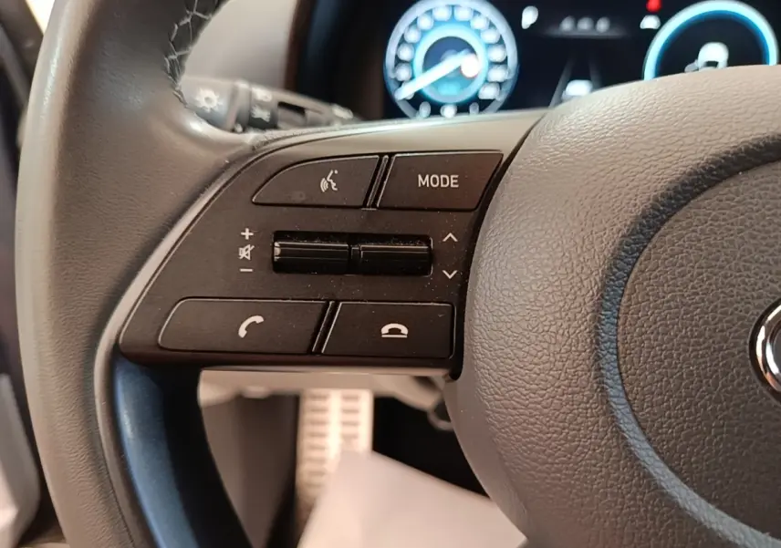 Gros plan sur le volant cuir gris foncé de la Hyundai Bayon 2023 avec commandes multimédia et tableau de bord numérique en arrière-plan.