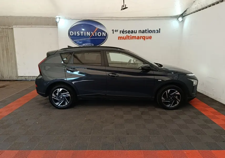 Vue latérale droite d'une Hyundai Bayon gris foncé 2023 avec jantes alliage et toit noir dans un showroom.