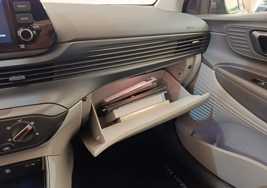 Vue intérieure côté passager du tableau de bord gris clair de la Hyundai Bayon 2023 avec boîte à gants ouverte contenant des documents.
