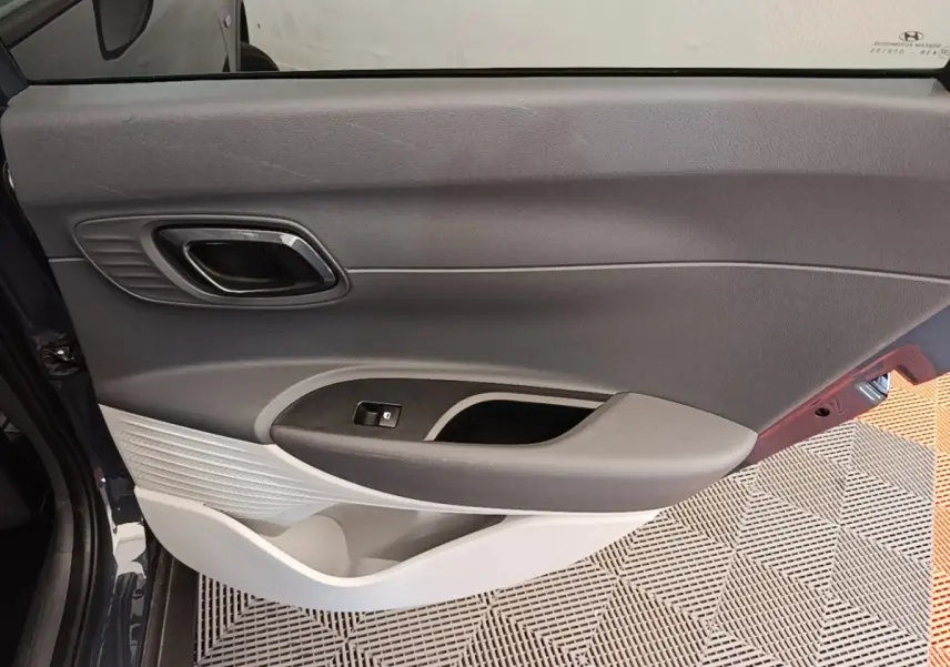 Vue rapprochée de la porte avant gauche gris foncé de la Hyundai Bayon 2023, avec poignée intérieure chromée et commande de vitre.