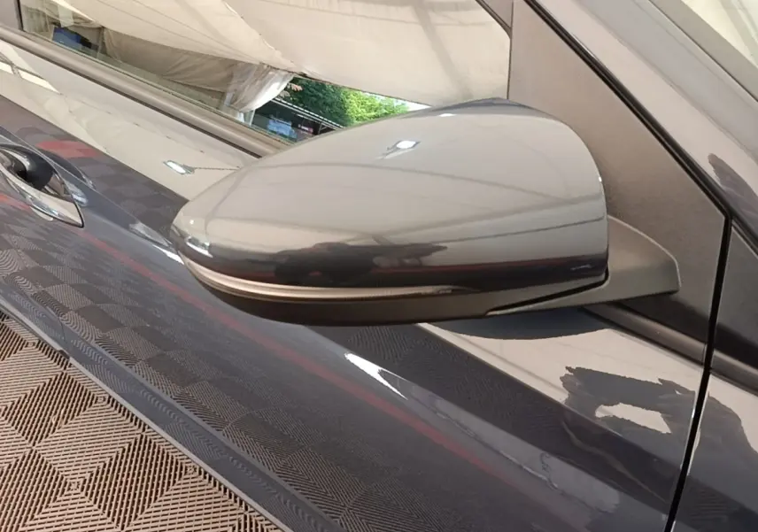 Gros plan sur le rétroviseur droit gris foncé d'une Hyundai Bayon 2023, avec reflet et poignée de porte visible.