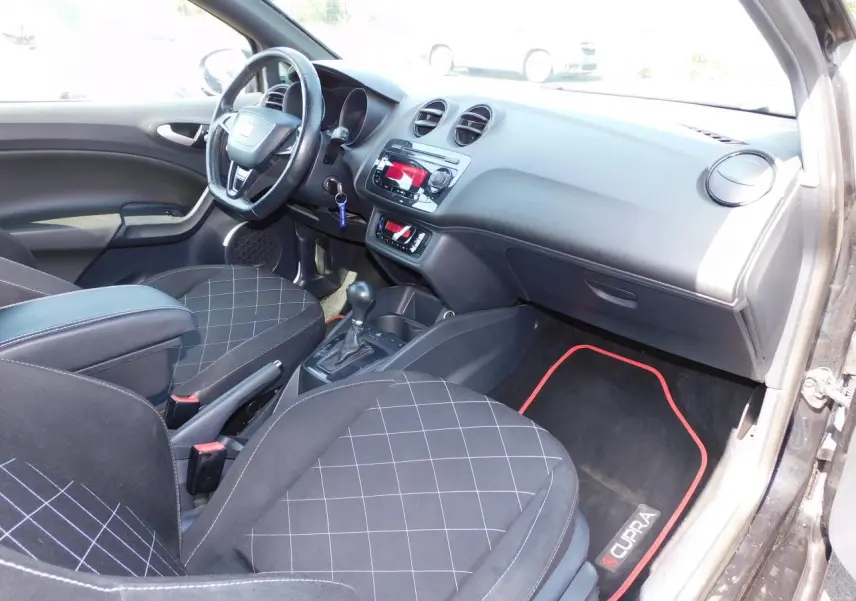 Intérieur avant droit de la SEAT Ibiza Cupra noire, sièges sport à motifs, volant cuir et tapis spécifiques Cupra rouges.