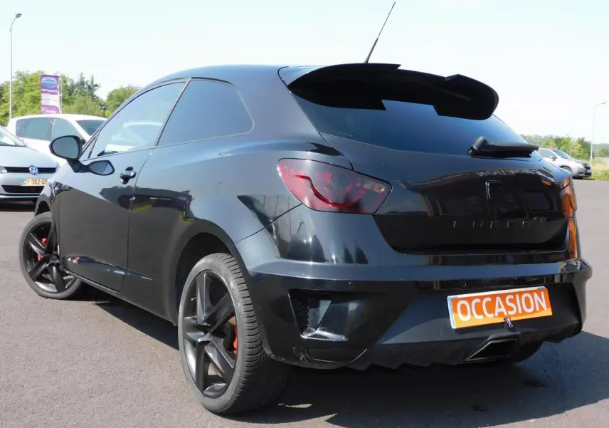 Vue 3/4 arrière droite d'une SEAT Ibiza Cupra noire avec jantes noires et sigle CUPRA sur le coffre.