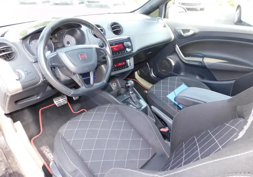 Intérieur de la SEAT Ibiza Cupra 2011 vu côté conducteur, sièges sport noirs avec surpiqûres blanches et volant cuir logoté.